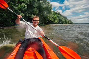 cheerful guy sits in   red kayak and row with a paddle