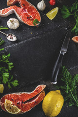 Raw salmon fish steaks with lemon, herbs, olive oil, ready for grill, slate cutting board, dark rusty background copy space