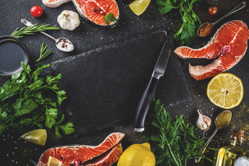 Raw salmon fish steaks with lemon, herbs, olive oil, ready for grill, slate cutting board, dark rusty background copy space