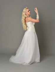 full length portrait of blonde  girl wearing white fantasy gown. standing pose in side profile,...
