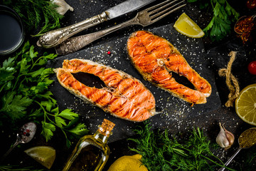 Grilled salmon fish steaks with ingredients lemon, herbs, olive oil, slate cutting board, dark rusty background copy space