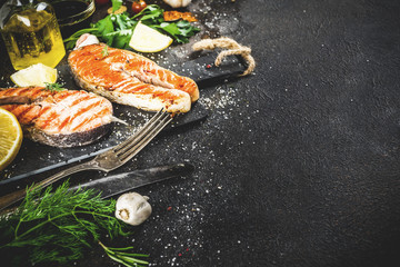 Grilled salmon fish steaks with ingredients lemon, herbs, olive oil, slate cutting board, dark rusty background copy space