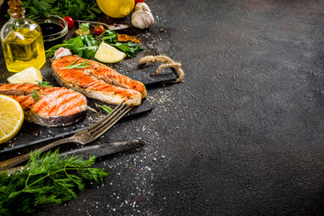 Grilled salmon fish steaks with ingredients lemon, herbs, olive oil, slate cutting board, dark rusty background copy space