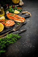 Grilled salmon fish steaks with ingredients lemon, herbs, olive oil, slate cutting board, dark rusty background copy space