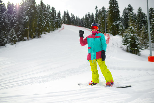 girl snowboarder in gear stands on a slope in the forest