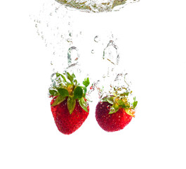  Red strawberries and cherries dropped into the water with splash on a white background