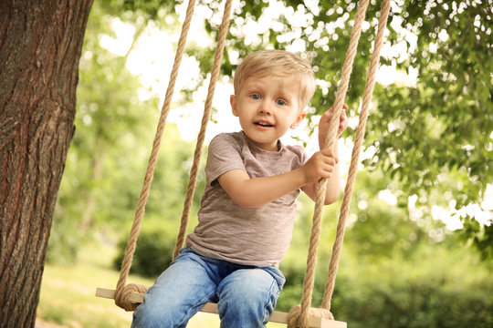 Cute little boy playing on swings in park