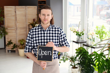 Fototapeta premium Male florist holding OPEN sign at workplace