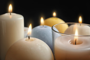 Fototapeta na wymiar Burning wax candles of different shapes and colors, closeup