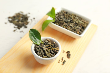 Wooden tray with dry tea and green leaves on table