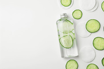 Flat lay composition with fresh cucumber skin care tonic and cotton pads on white background