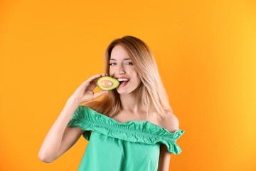 Portrait of young beautiful woman with ripe delicious avocado on color background