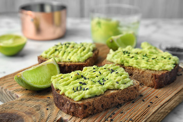 Crisp rye toasts with avocado on wooden board, closeup