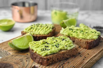 Poster Crisp rye toasts with avocado on wooden board, closeup © New Africa