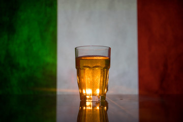 Creative concept. Pint of fresh beer on grass with blurred flag of Italy on background or Glass of lager beer ready for drink. Copy space.
