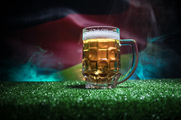 Creative concept. Pint of fresh beer on grass with blurred flag of Germany on background or Glass...