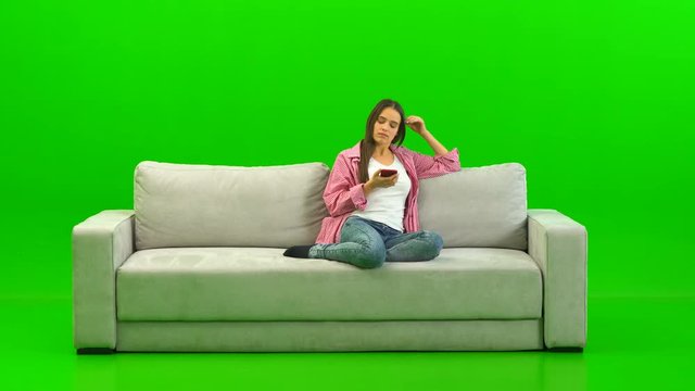 The woman phones on the sofa on the green background