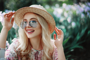 Outdoor close up portrait of beautiful young happy smiling woman wearing blue sunglasses, straw hat...