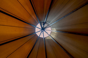 Looking up towards the smoke hole window teepee-ceiling from inside the tent shows bright day light filtering in creating a cozy ambience in the alternate lodging for glamping or outdoor adventurers
