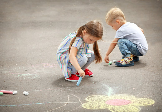Cute little children drawing with chalk on asphalt