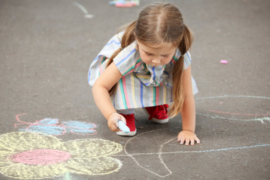 Cute little girl drawing with chalk on  asphalt