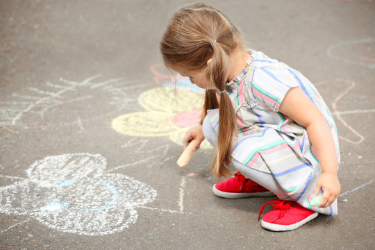 Cute little girl drawing with chalk on  asphalt