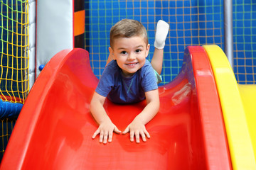 Fototapeta na wymiar Little boy riding on slide in entertainment center