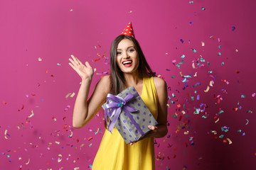 Young woman with birthday gift on color background