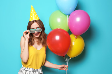 Young woman with bright balloons on color background. Birthday celebration