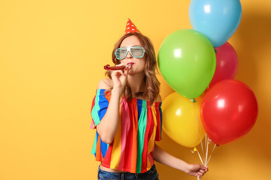 Young woman with bright balloons and party blower on color background. Birthday celebration