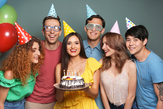 Young people celebrating birthday with tasty cake on color background
