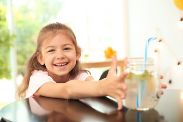 Little girl with natural lemonade at table indoors