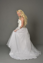 full length portrait of blonde girl wearing white gown, standing pose with back to the camera. grey studio background.