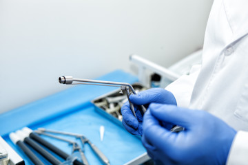 The doctor's hand holds the ligator for the treatment of hemorrhoids against the background of blurred medical instruments in the operating room