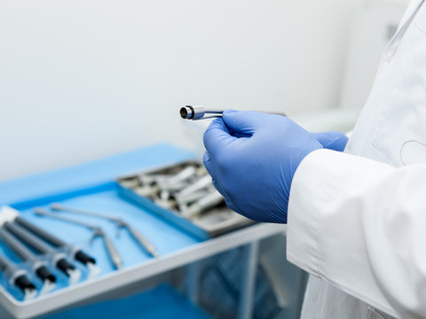 The doctor's hand holds the ligator for the treatment of hemorrhoids against the background of blurred medical instruments in the operating room
