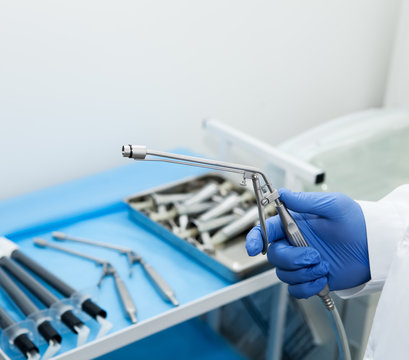The doctor's hand holds the ligator for the treatment of hemorrhoids against the background of blurred medical instruments in the operating room