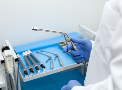 The doctor's hand holds the ligator for the treatment of hemorrhoids against the background of blurred medical instruments in the operating room