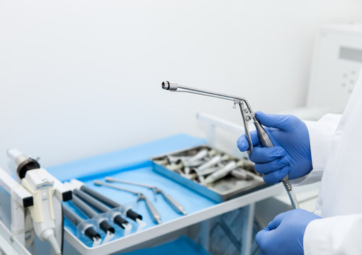 The doctor's hand holds the ligator for the treatment of hemorrhoids against the background of blurred medical instruments in the operating room
