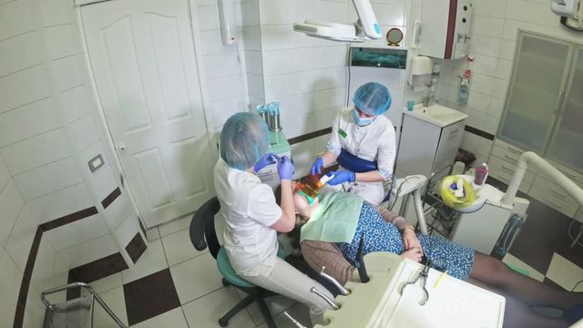 Woman at dentist clinic gets dental treatment to fill a cavity in a tooth. Dental restoration and composite material polymerization with UV light and laser. Shooting at a wide angle.