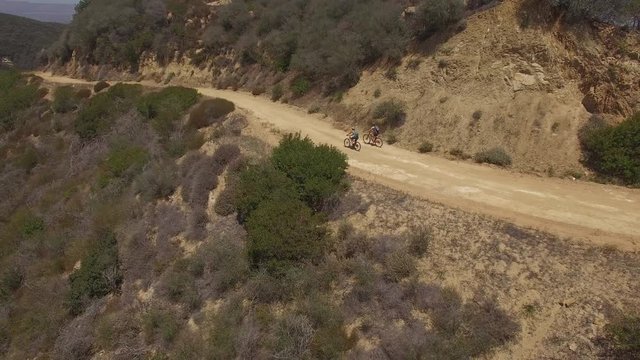 Aerial of cyclists riding along dirt road on the cliff of a mountain