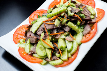 Chinese cuisine, boiled beef with cucumber and tomato in white plate on black background