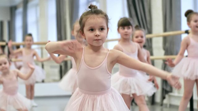 Tilt down shot of adorable little girl dancing and jumping when having ballet lesson, medium shot