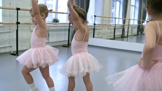 Tilt up shot of little girls in leotards and tutu skirts walking with their hands up in the air during ballet lesson