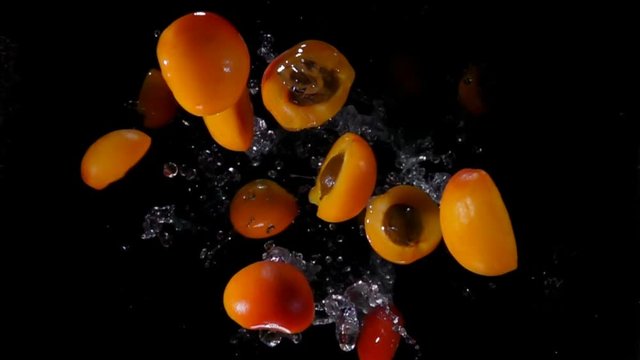 Halves ripe apricots with water bouncing against to the camera on a black background in slow motion
