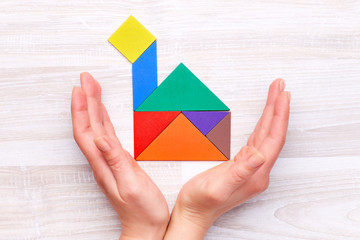 From above shot of hands person protect tangram figures into shape of house on wooden table.