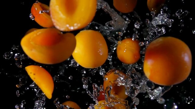 Halves ripe apricots with water bouncing against to the camera on a black background closeup in slow motion