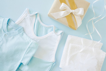 New, light blue baby clothes and box with white ribbon on the pastel blue table. Soft colors. Giving or receiving gifts at baby shower party.