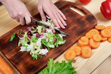 Female hands chopping green salad , cooking vegetables salad on wooden background