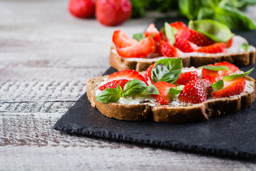 Strawberry bruschetta with cottage cheese,basil and strawberry on slate board on shabby wooden table background, copy space