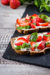 Strawberry bruschetta with cottage cheese,basil and strawberry on slate board on shabby wooden table background